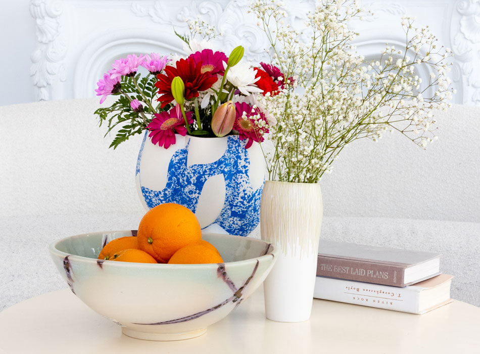 A collection of bowls and vases with flowers and oranges on a white table