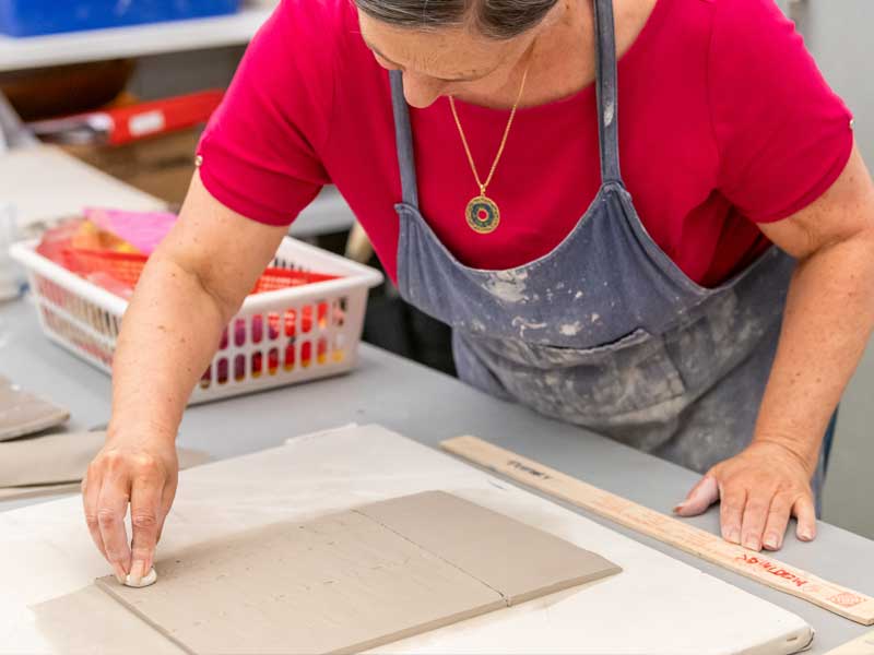 A woman in the studio stamping a slab of clay