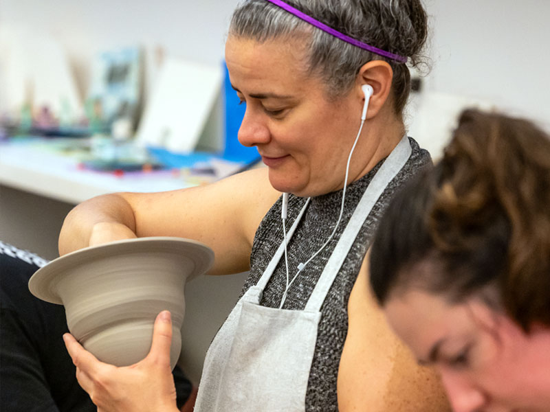 A woman wearing an apron and making a clay bowl