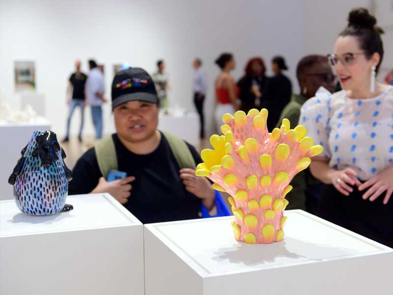 Two people looking at colourful ceramic sculptures on plinths