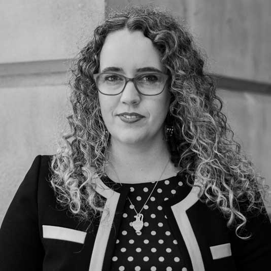 A black and white portrait of Dr. Caroline McCaffrey-Howarth wearing a polka dot shirt and cardigan