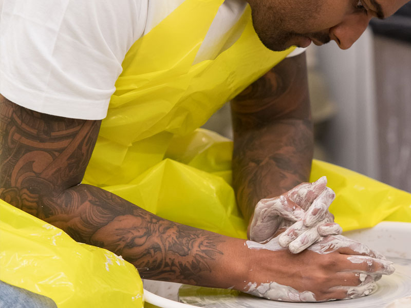 A man wearing a yellow apron using the pottery wheel