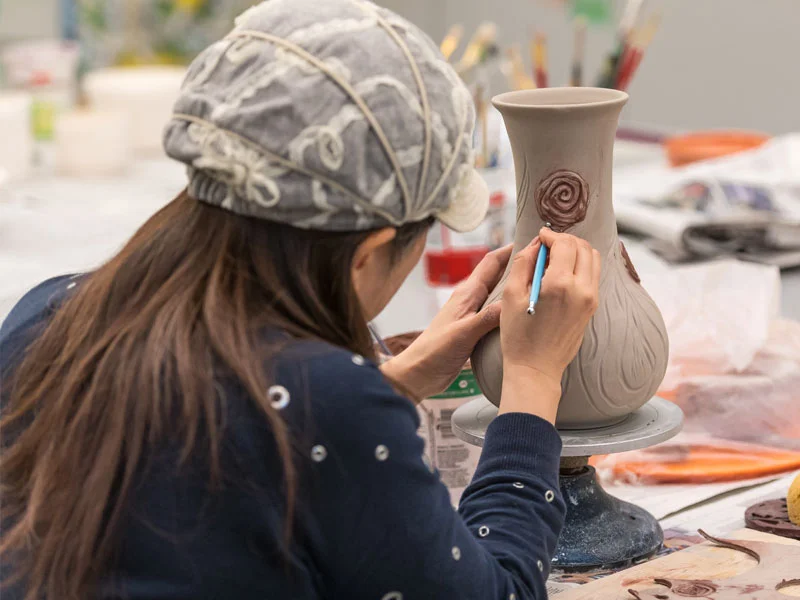 A woman shown from behind working on a clay vessel