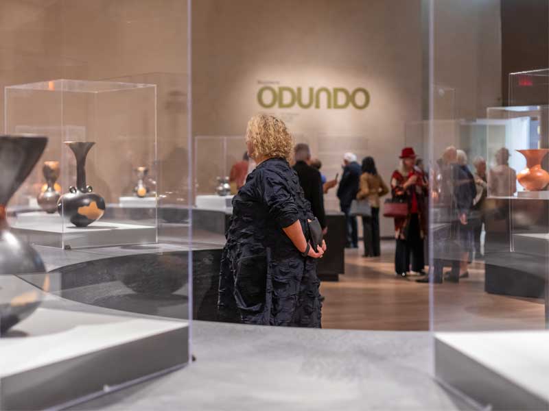 A woman looking at ceramic vessels on plinth with more visitors in the background