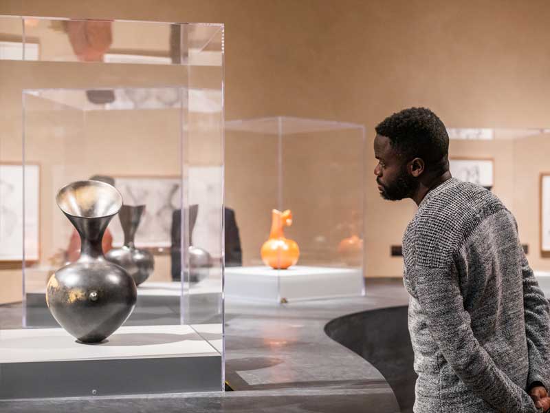 A man looking at a vessel by Magdalene Odundo in a glass case