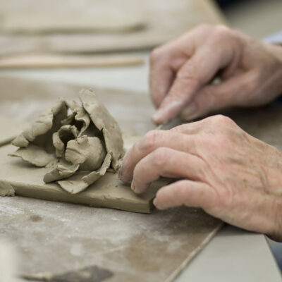 Hands shaping a rose out of clay