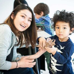Child holding a clay dinosaur next to a woman smiling