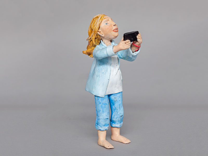 Miniature polymer clay figure of a woman looking at a cell phone