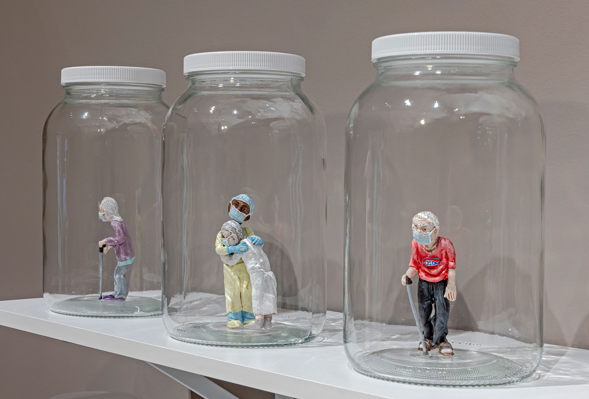 A shelf with glass mason jars containing miniature polymer clay figures of elderly people and healthcare workers