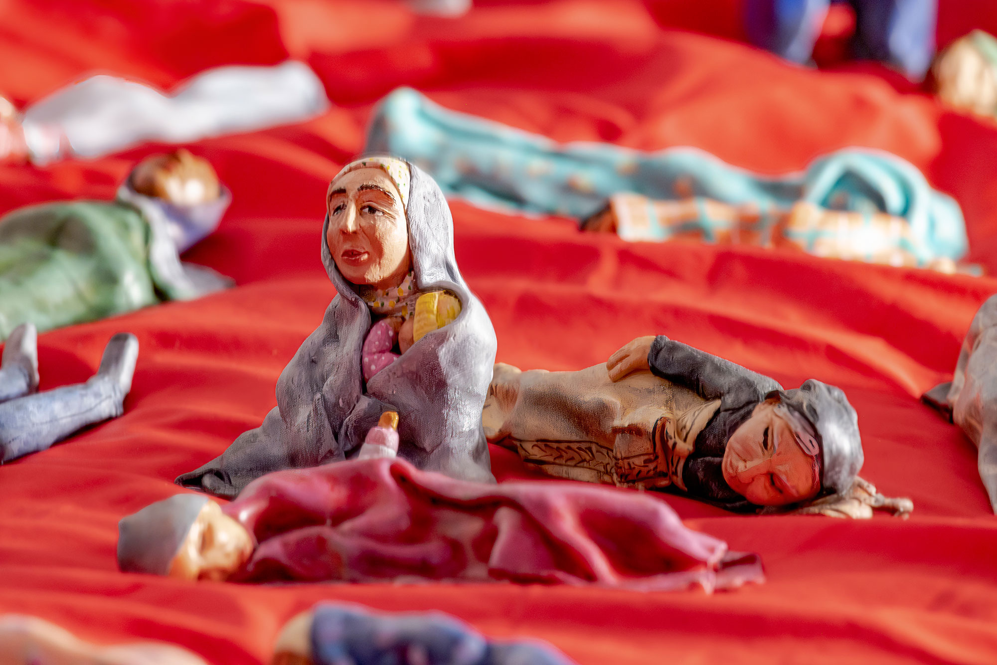 Miniature polymer clay figures depicting people experiencing homelessness lying on a red sleeping bag
