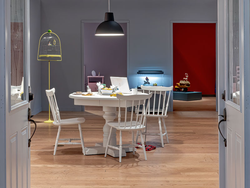 Installation view of Housewarming with a kitchen table and chairs visible inside a set of open doors