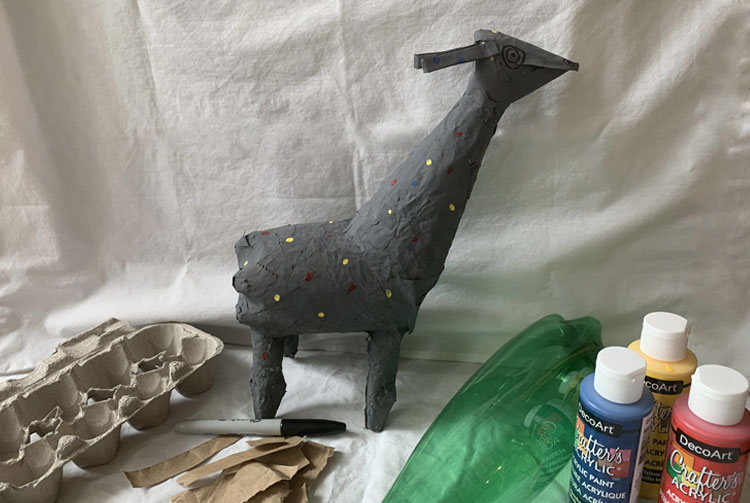 Llama-like paper mache creature surrounded by art materials