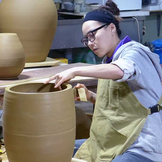 Artist Grace Han sculpting a large vessel on the wheel in a studio