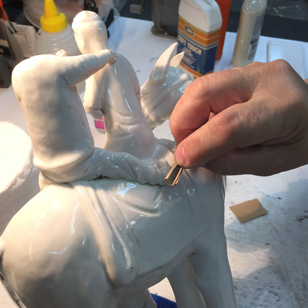 Hand smoothing the foot of a white porcelain figure on horseback