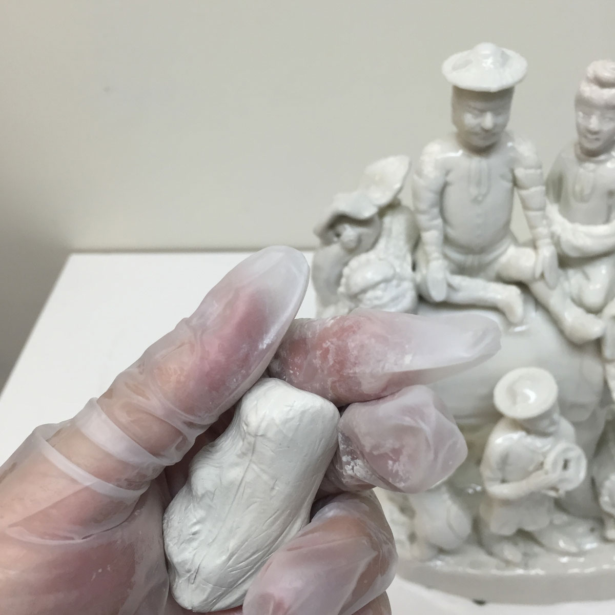 Hand squeezing clay with white porcelain figure in the background