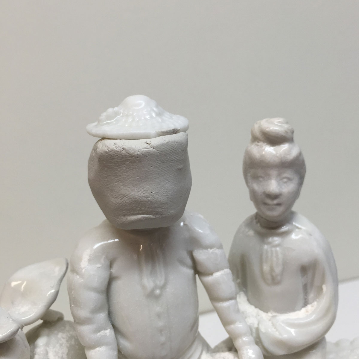 Two white porcelain figures, one with an clay mould on its face