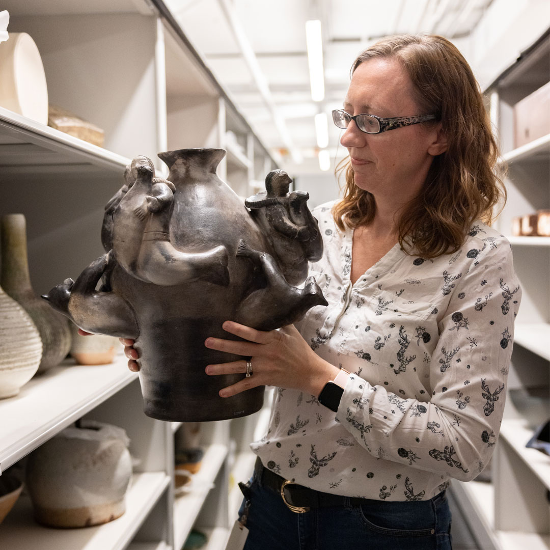 Collections Manager Christina Macdonald in storage holding a large Inuit ceramic vessel