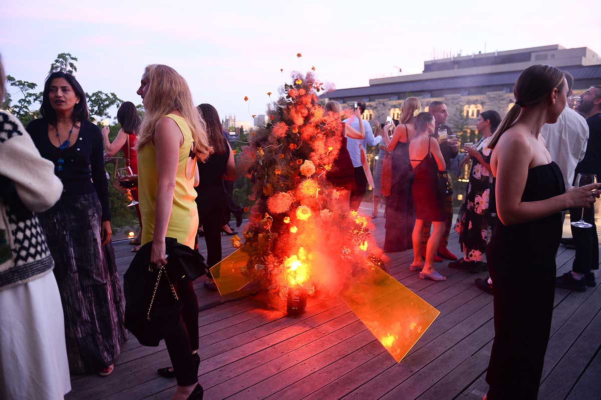 Party goers on the terrace surrounding a floral sculpture with orange lighting