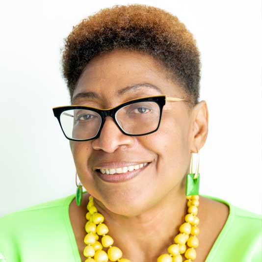 Portrait of artist Jacqueline Bishop wearing a bright green top and yellow beaded necklace