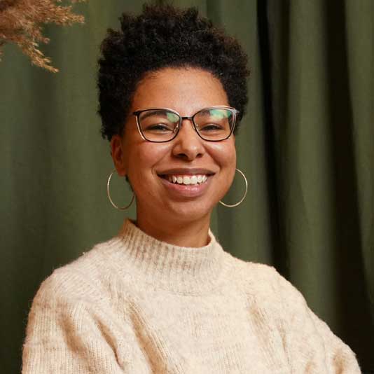 A Black woman with glasses smiling at the camera