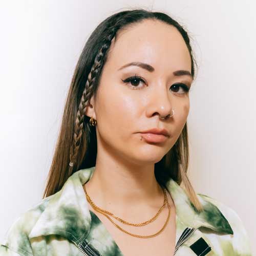 Portrait of DJ Jayemkayem wearing a green and white collared shirt on a white backfround