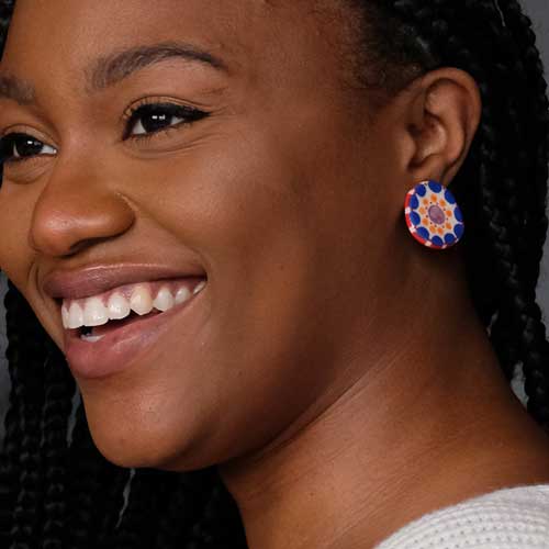A woman smiling wearing a round blue, red, and orange ceramic earring