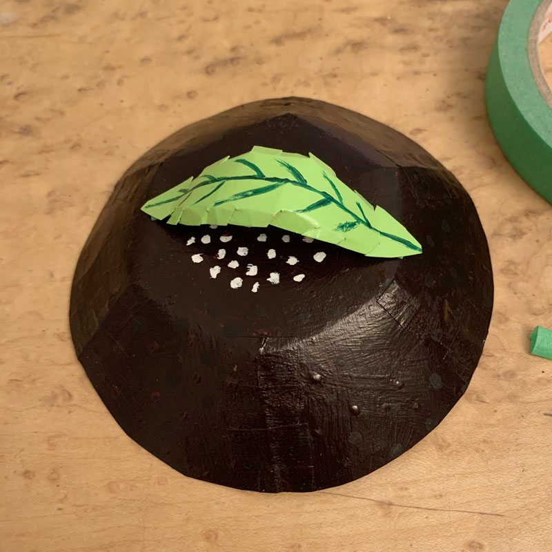 Paper bowl painted dark green with a handle in the shape of a leaf