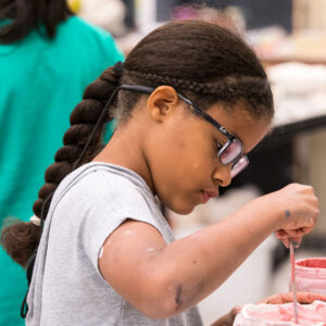 A child with a long braid and glasses glazing ceramics