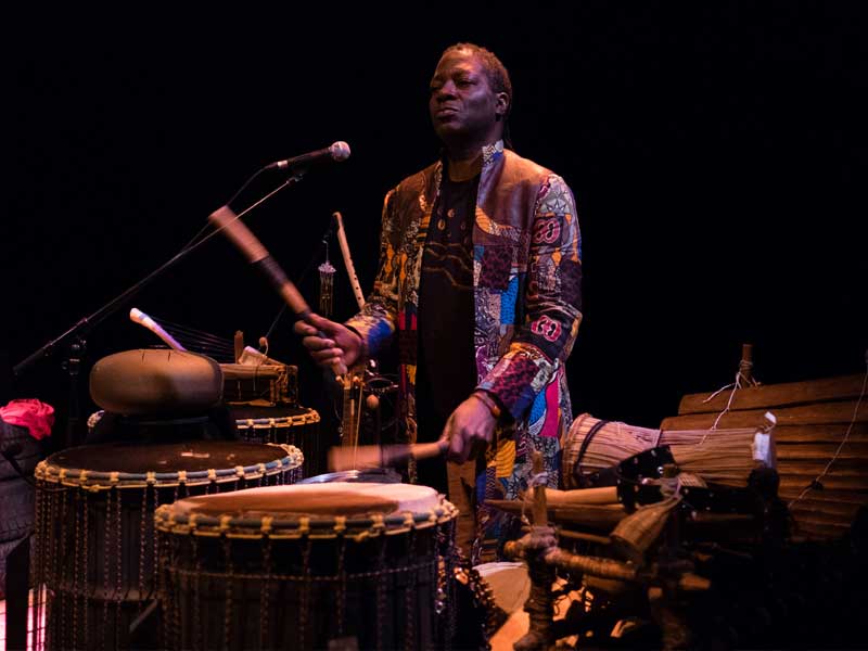 Kobèna Aquaa-Harrison surrounded by instruments and playing drums