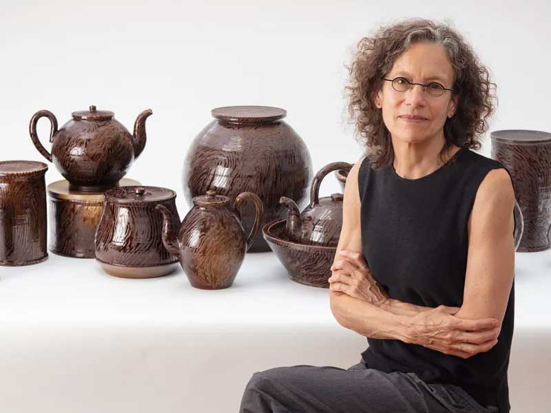 Artist Linda Sikora seated in front of her ceramic vessels