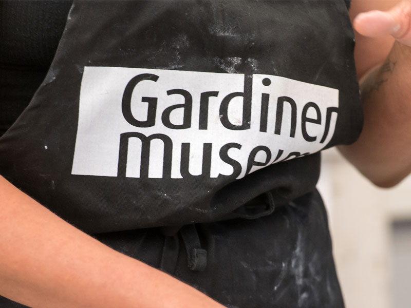 A person wearing an apron with a Gardiner Museum logo