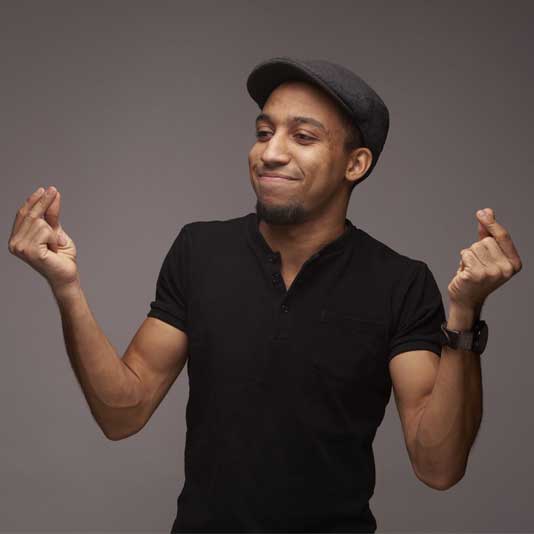 Luke Reece wearing a black polo shirt and hat, snapping his fingers