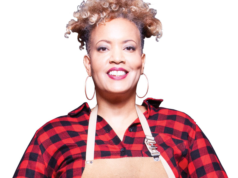 Roxanne Brathwaite pictured from the chest up, wearing a red plaid shirt and an apron