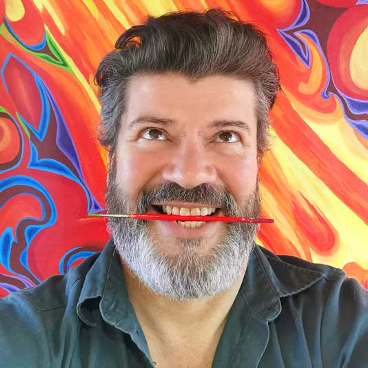 Artist Michel Dumont with a paintbrush between his teeth and standing against a colourful background