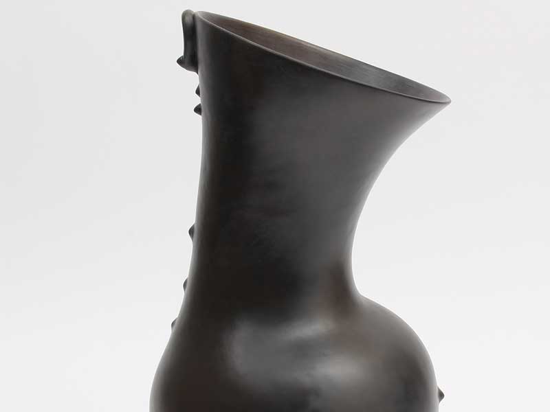 Details of a black ceramic vessel with a round belly and flared neck