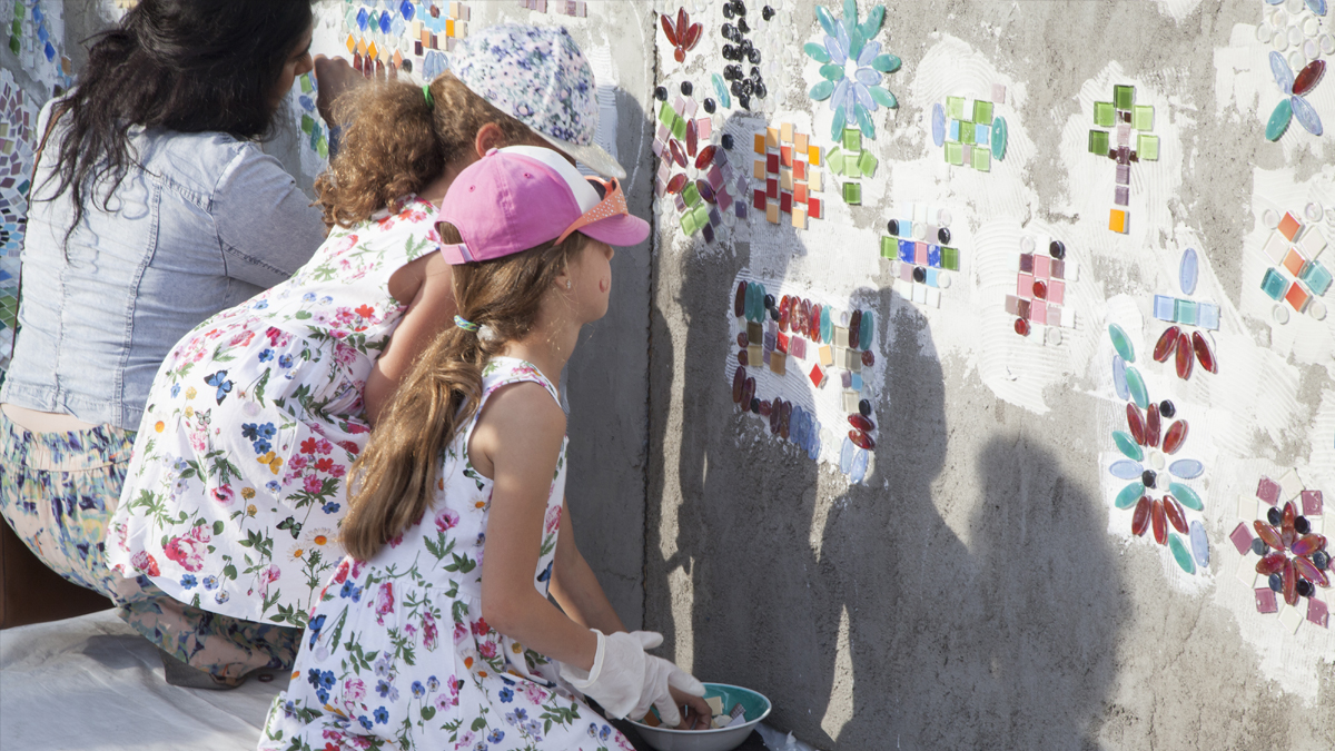 Two girls putting colourful tiles on a concrete wall