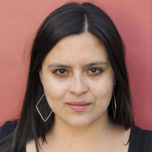 Headshot of Pamela Cevallos from the shoulders up. She has long dark hair and is wearing geometric earrings and a black shirt.