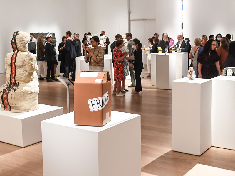 People dressed in cocktail attire mingling and looking at ceramic art