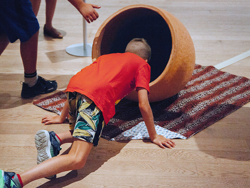 A child on all fours looking into a large ceramic vessel