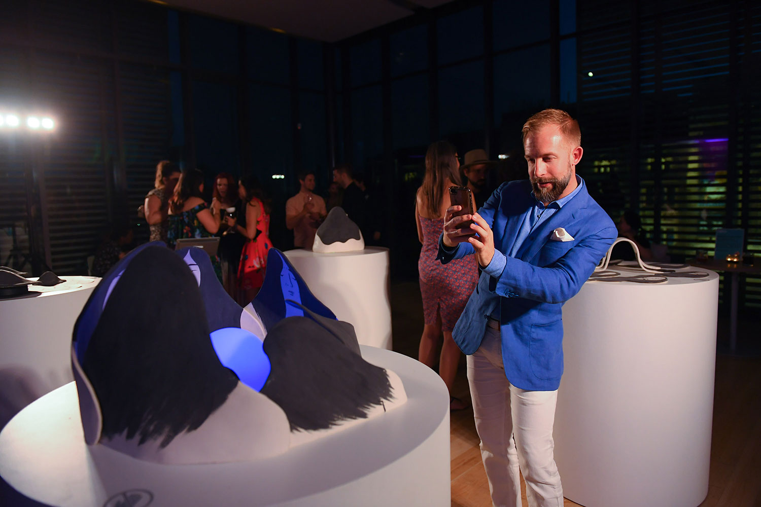 A party-goer in a blue suit jacket taking a photo of artwork by Ness Lee on a plinth