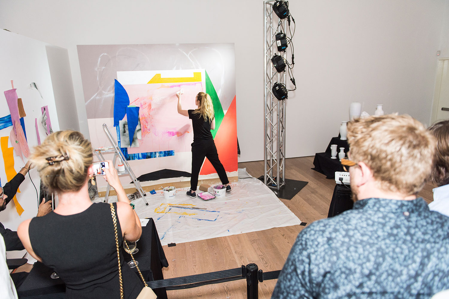 A woman with a blond ponytail live painting while people watch