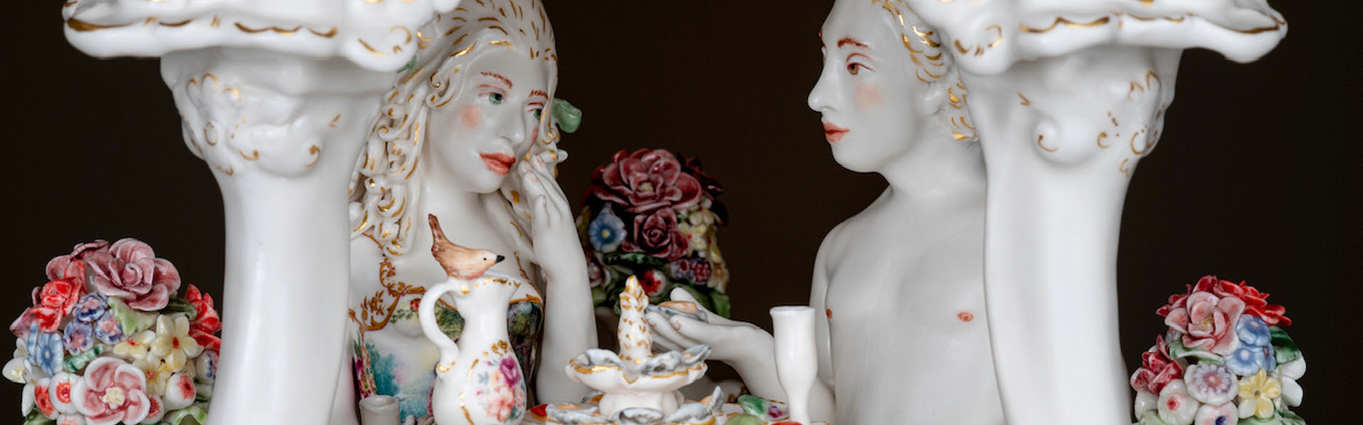 Image of two white porcelain figurines at a dining table surrounded by flowers