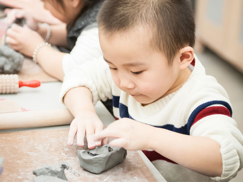 A little boy wearing a white sweater and working with clay