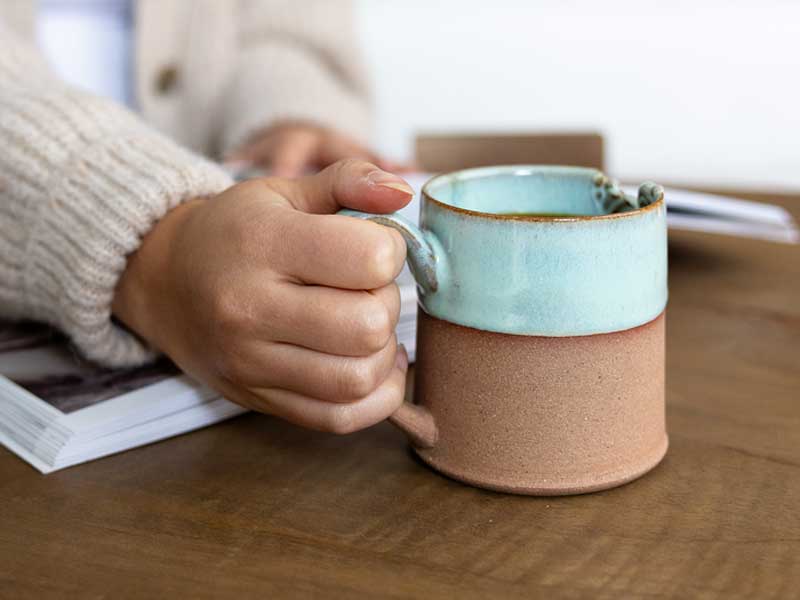 Hand holding a brown and turquoise ceramic mug