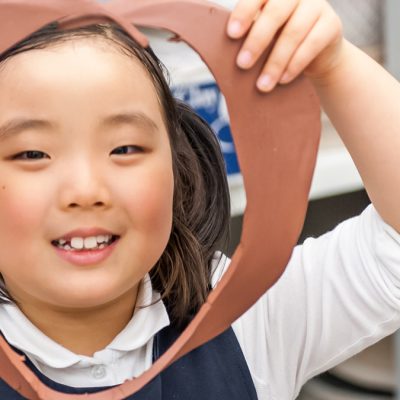 Young girl holding a circular piece of clay with a cutout in front of her face