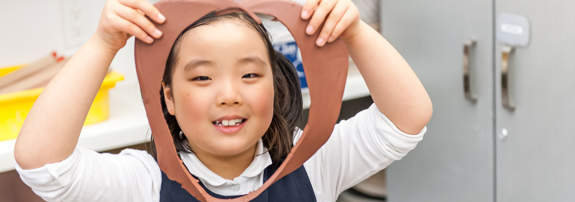 Young girl holding a circular piece of clay with a cutout in front of her face