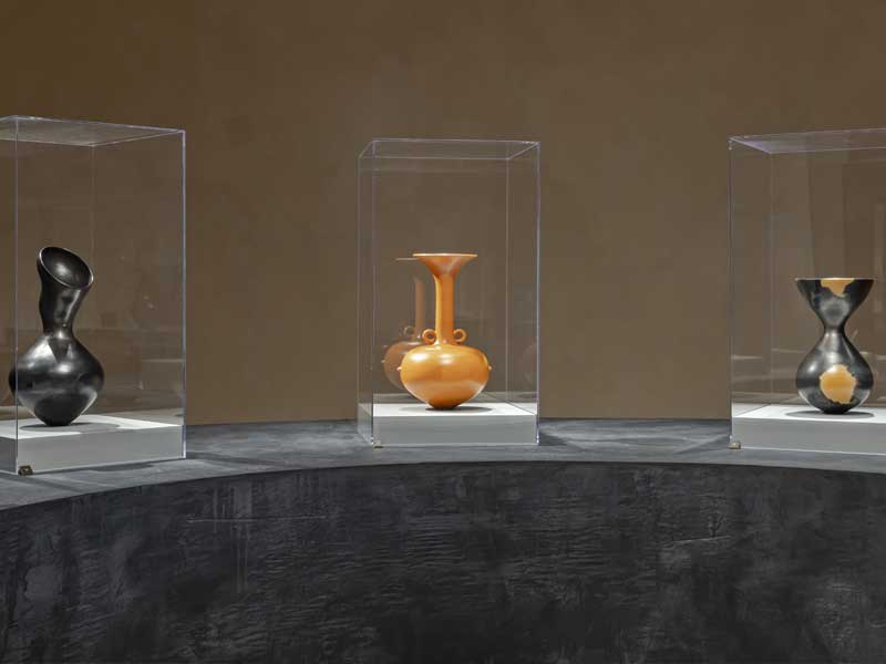 Three ceramic vessel in black and orange on a black plinth