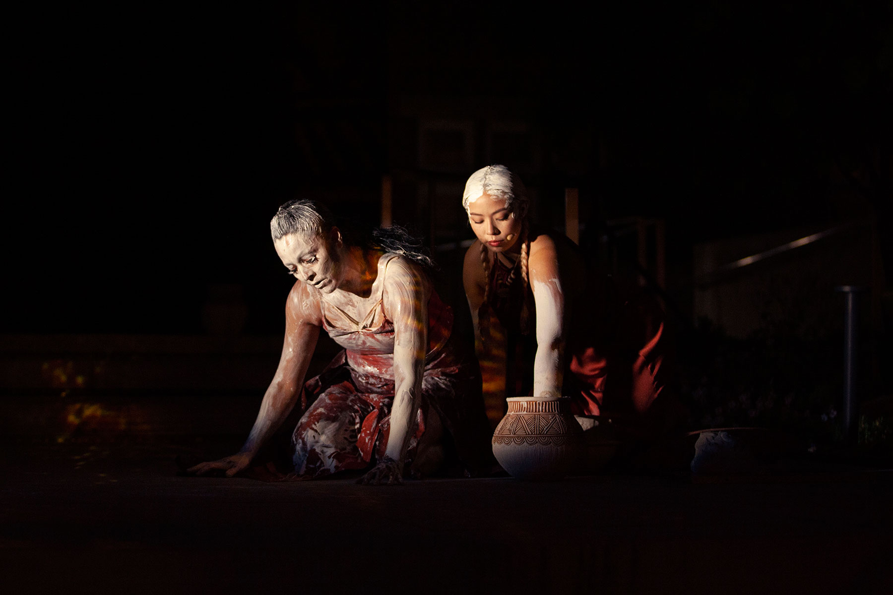 Two Indigenous women kneeling down together and covered in clay