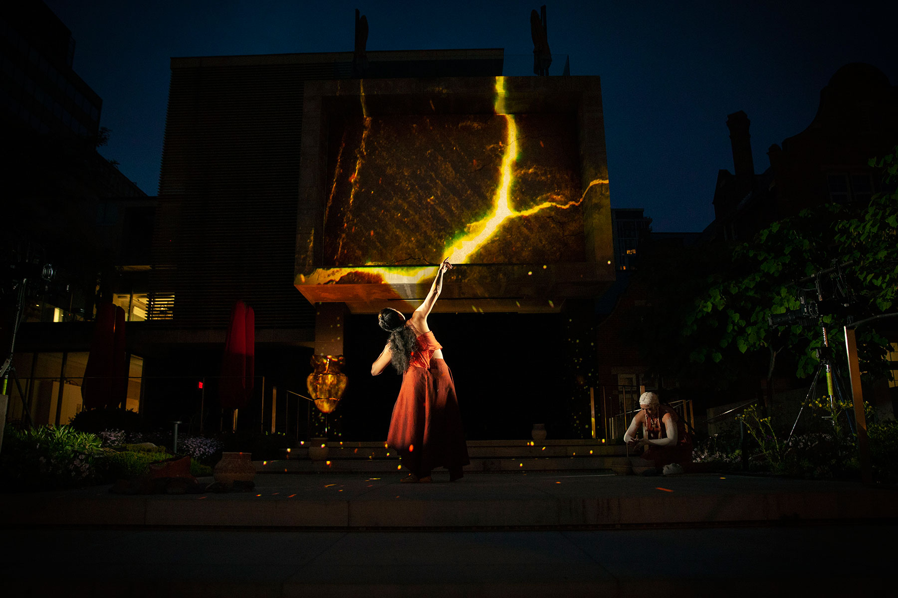 An Indigenous dancer reaching her hand up toward the projection of a lightening bolt