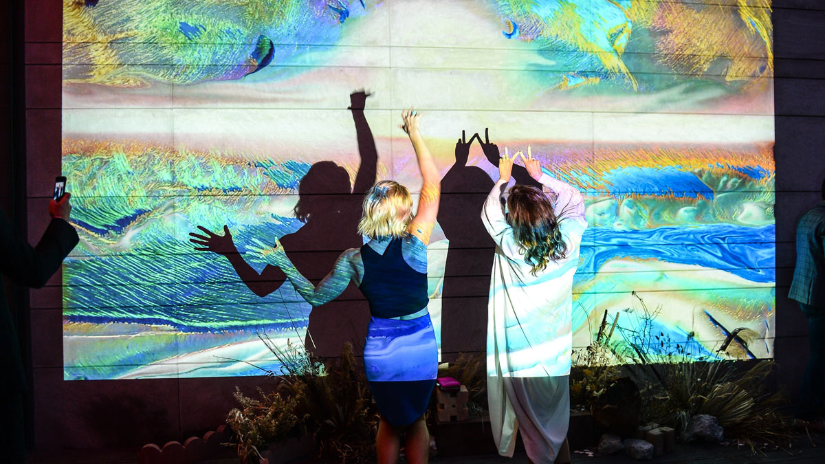 Two party guests in front of a digital landscape installation with their backs to the camera